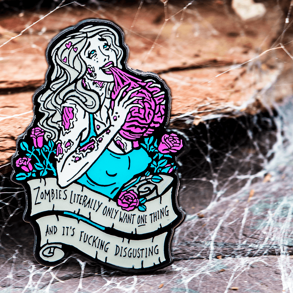 A cyan, magenta, white, black, and grey enamel pin of a buxom female zombie eating a human brain