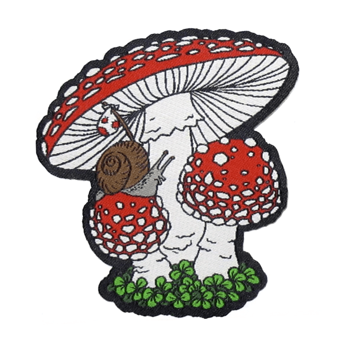 A woven patch, featuring a brown and grey snail carrying a bindle as he crawls over a trio of red and white Amanita muscaria agaric mushrooms and a patch of green moss.