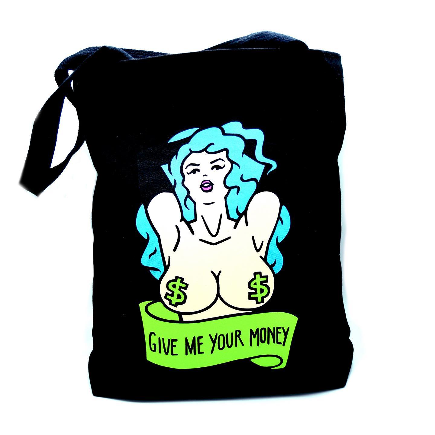 A black canvas tote bag, featuring the bust of a topless, blue haired woman wearing green dollar sign pasties. Below her is a banner that says "GIVE ME YOUR MONEY".