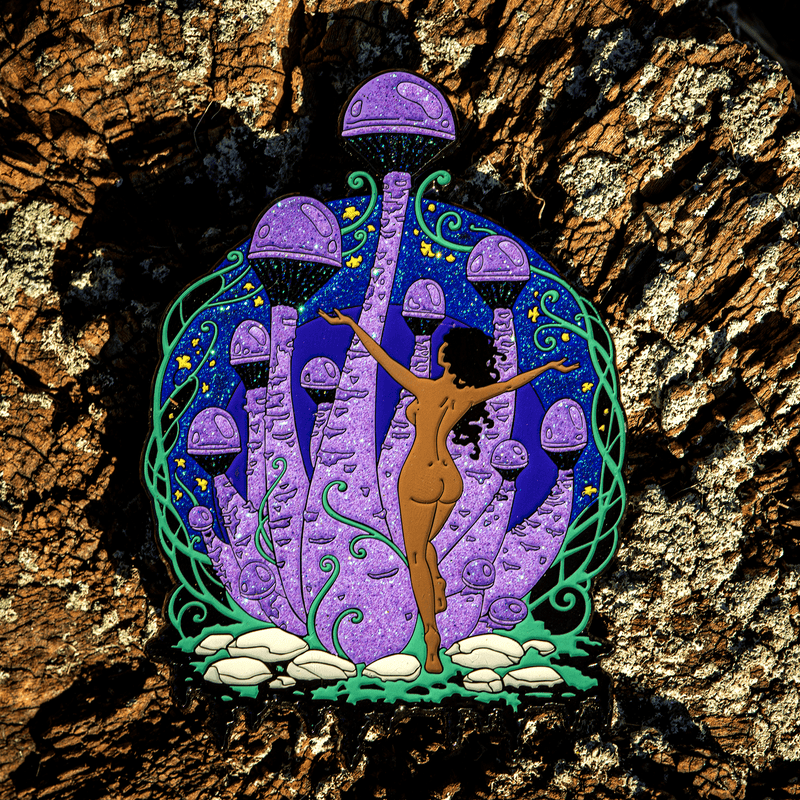 A large enamel pin of a Black woman with curly dark hair dancing in front of giant mushrooms, with glittering dark blue and violet tones.
