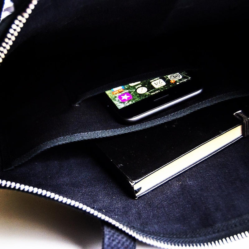 A view inside the unzipped Rover Ita Pin Tote, showing inner panels and a cell phone pocket.