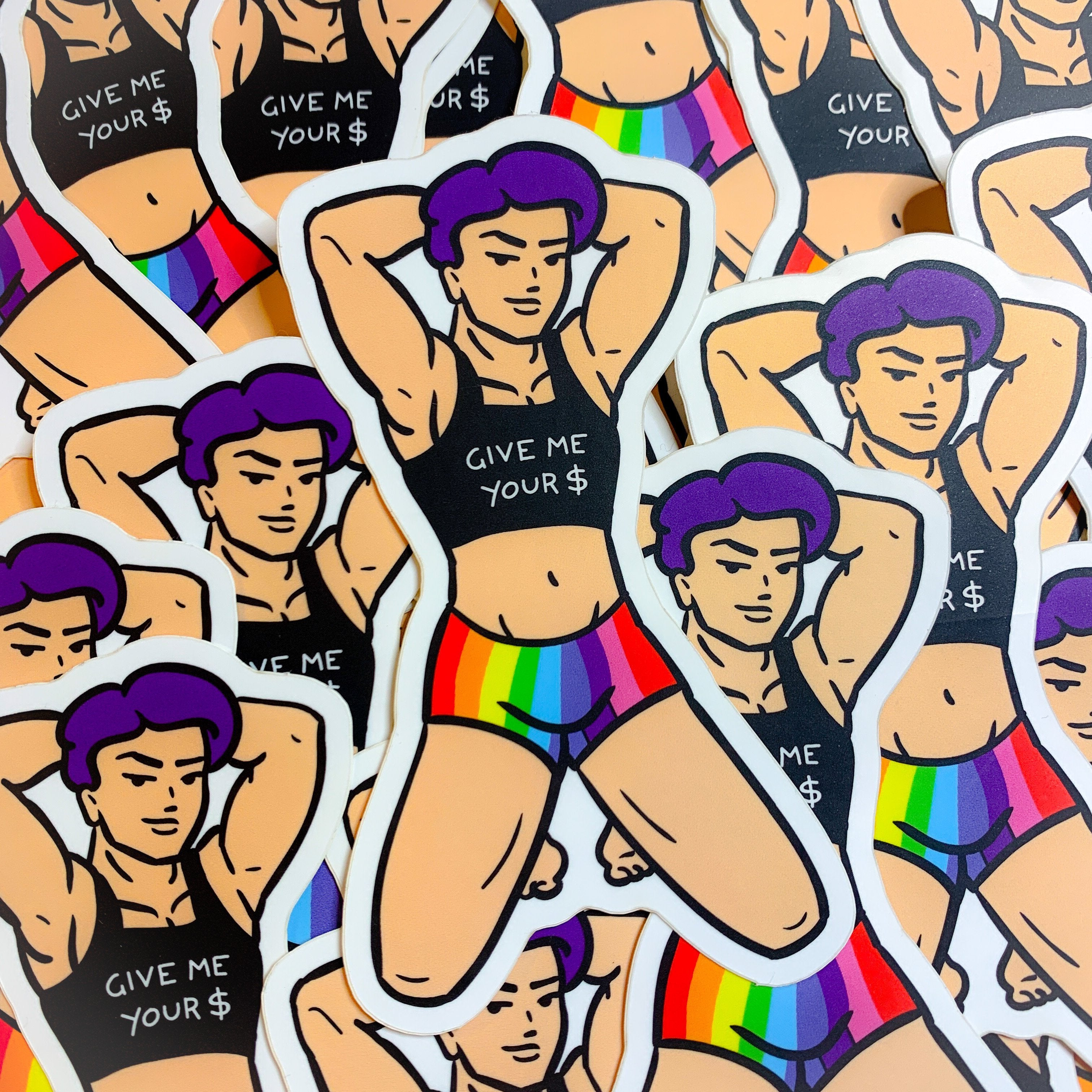 Payton stickers laid out together on a table. Payton is a muscular masculine person, with rainbow shorts and a black midriff tank that says "GIVE ME YOUR $". He is posed confidently on his knees, with his hands behind his purple hair, and a slight smile.
