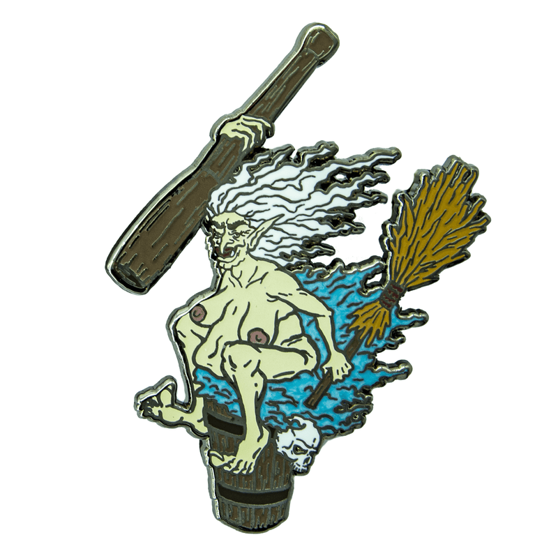 An enamel pin of Baba Yaga the crone witch, riding her mortar and pestle with broom in hand. She has taken off her clothing and sits on it with a wicked smile. She has greenish white skin and white hair, and her discarded clothing is blue.