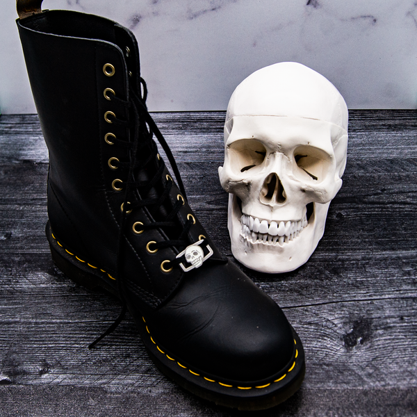 A classic black Doc Marten boot displaying a skull shoelace charm neck to a model of a human skull.