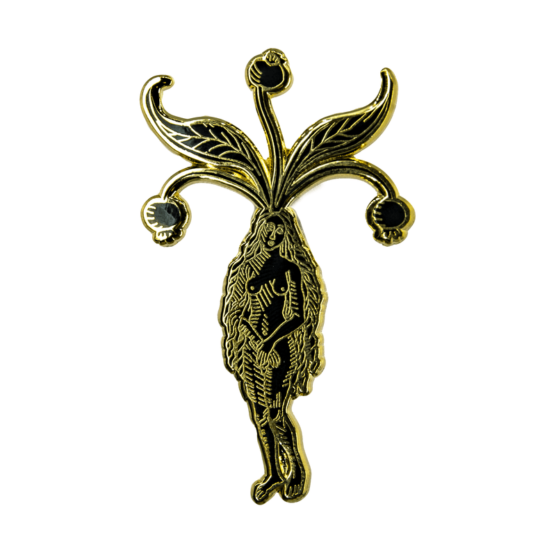 A black and gold enamel pin of a nude woman with long hair and mandrake leaves and berries sprouting from her head.