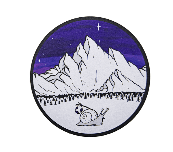 A kraft paper sticker of a white snail carrying a bindle across a snowy winter landscape, with black pine tree silhouettes, icy white mountains, and a blue and purple starry night sky in the background.